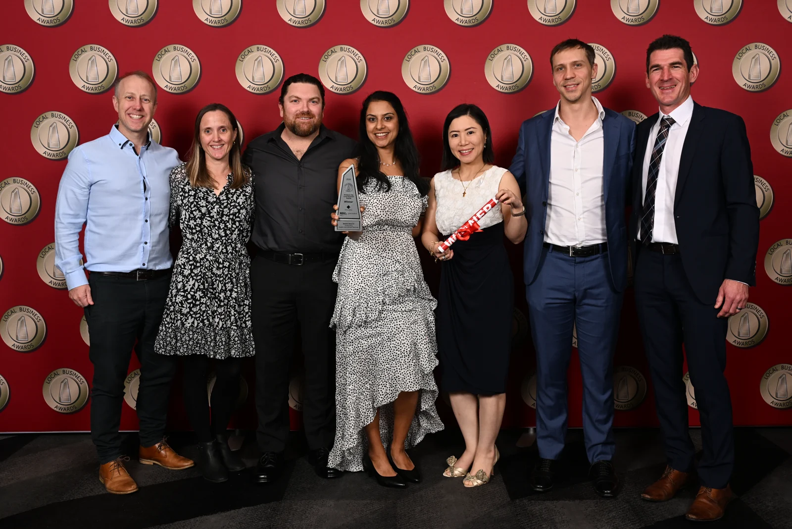 The Modia Health group celebrating with the award against the red Local Business Awards backdrop.
