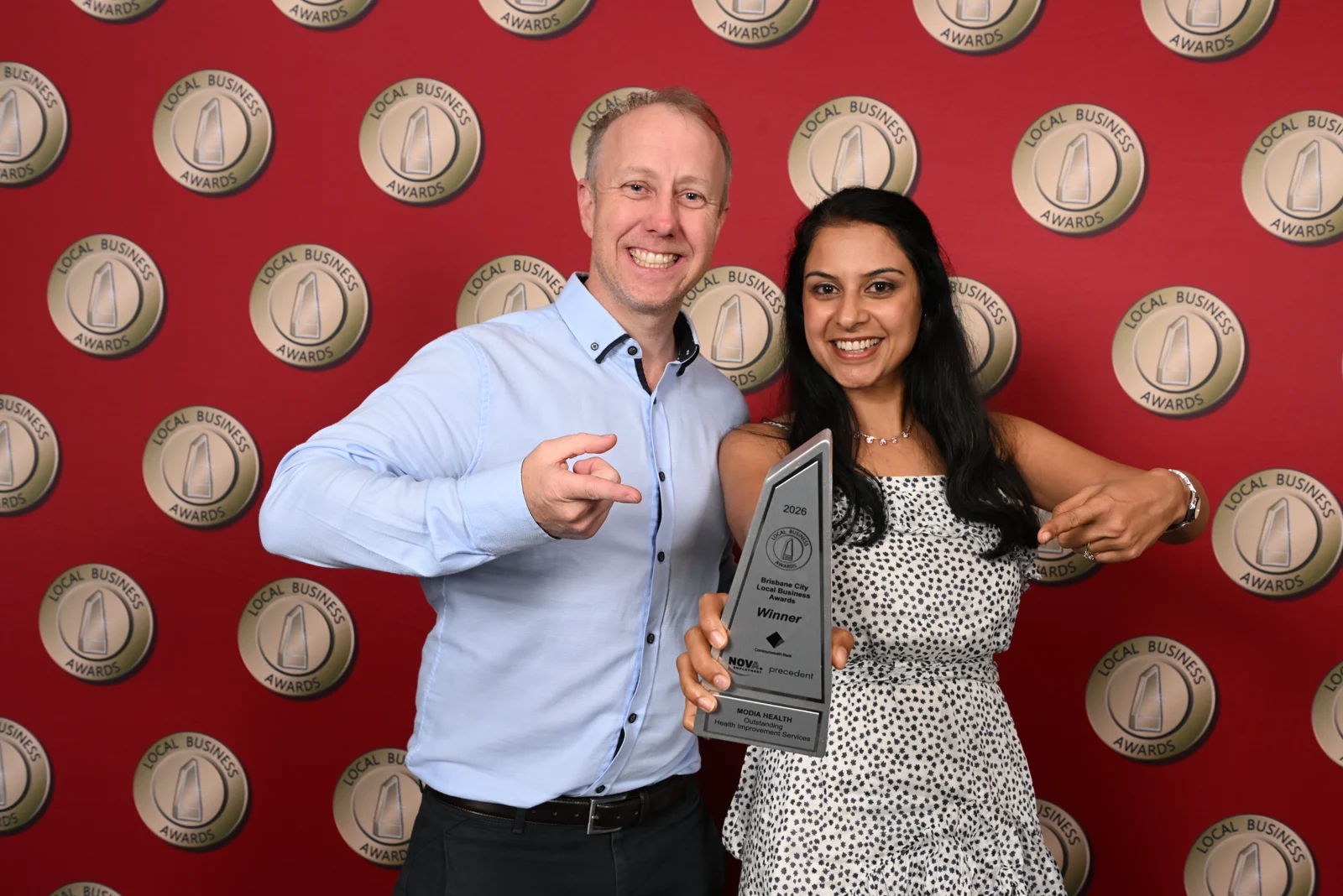 Two members of the Modia Health awards group smiling and pointing to the 2026 winner’s trophy.